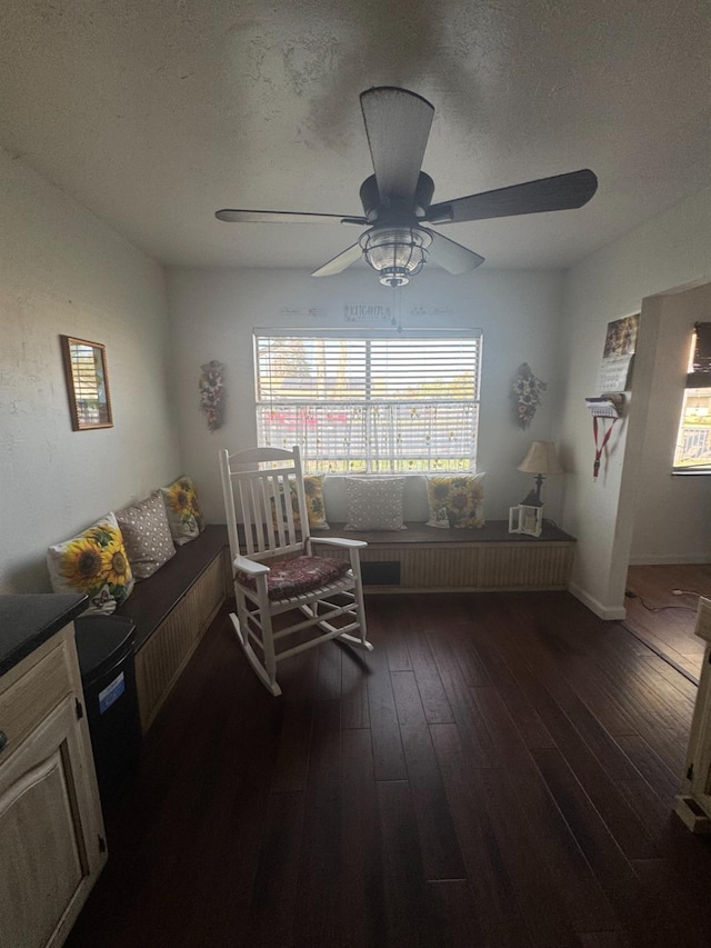 living area featuring a textured ceiling, dark wood-type flooring, and a ceiling fan