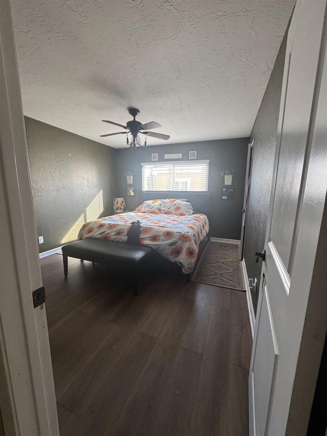 bedroom with a textured ceiling, a textured wall, a ceiling fan, baseboards, and wood-type flooring