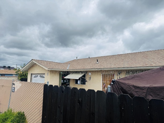 view of front of property with roof with shingles, fence, and stucco siding