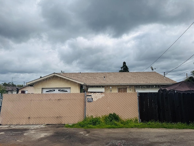 view of front of home featuring a garage, a fenced front yard, roof with shingles, and stucco siding