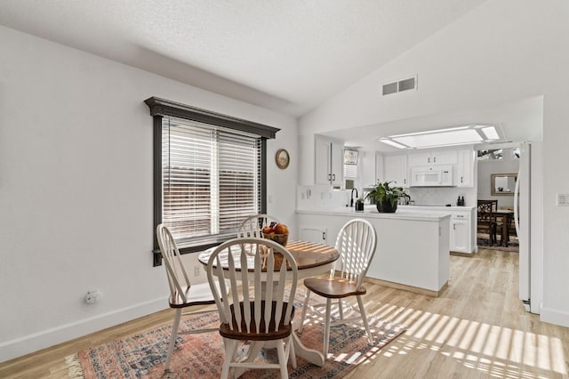 dining space featuring lofted ceiling, light wood-style flooring, visible vents, and a healthy amount of sunlight