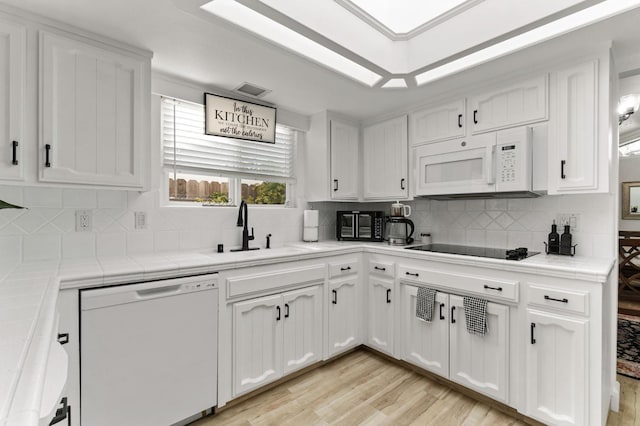 kitchen with white appliances, tile counters, white cabinets, and a sink