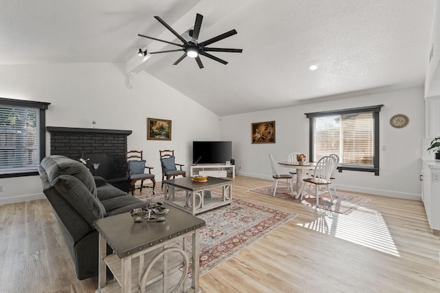 living room featuring vaulted ceiling with beams, light wood-style flooring, a fireplace, and baseboards