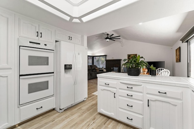 kitchen with white appliances, tile counters, white cabinets, lofted ceiling, and light wood-style floors