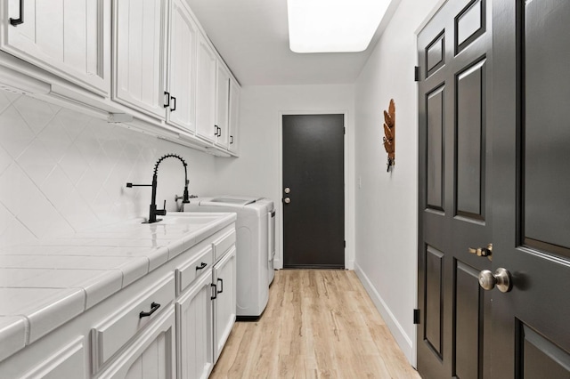 laundry area with washing machine and dryer, a sink, baseboards, light wood-type flooring, and cabinet space