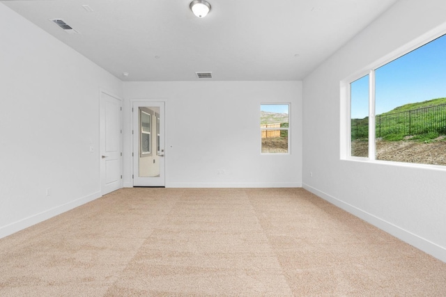 empty room featuring light colored carpet, visible vents, and baseboards
