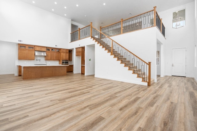 unfurnished living room featuring light wood finished floors, baseboards, a high ceiling, and stairway