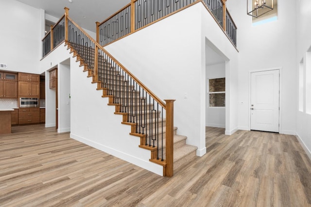 foyer with light wood-type flooring, a towering ceiling, baseboards, and an inviting chandelier