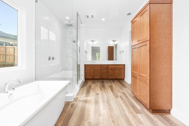 full bathroom with visible vents, wood finished floors, vanity, a freestanding tub, and a shower stall