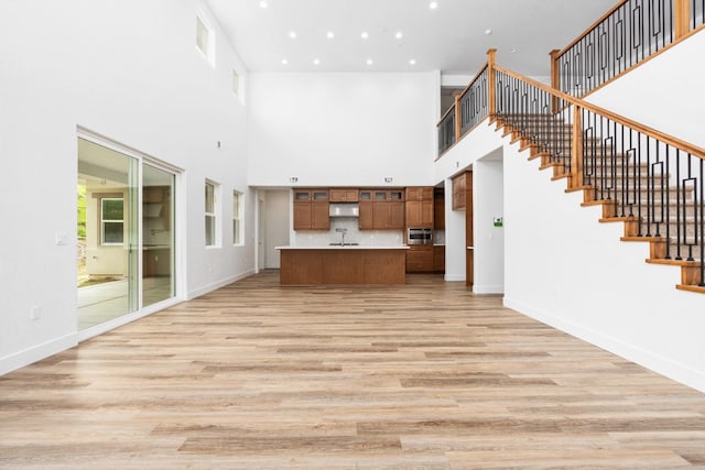 unfurnished living room featuring recessed lighting, a sink, baseboards, stairs, and light wood-type flooring
