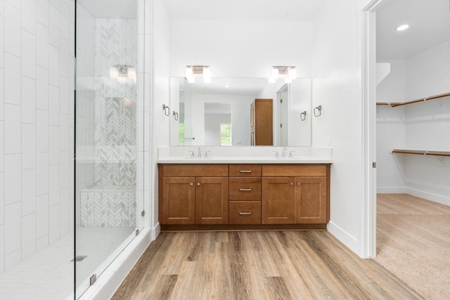 full bath featuring double vanity, wood finished floors, walk in shower, and a sink