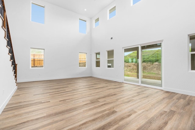 unfurnished living room featuring baseboards, light wood finished floors, and stairs
