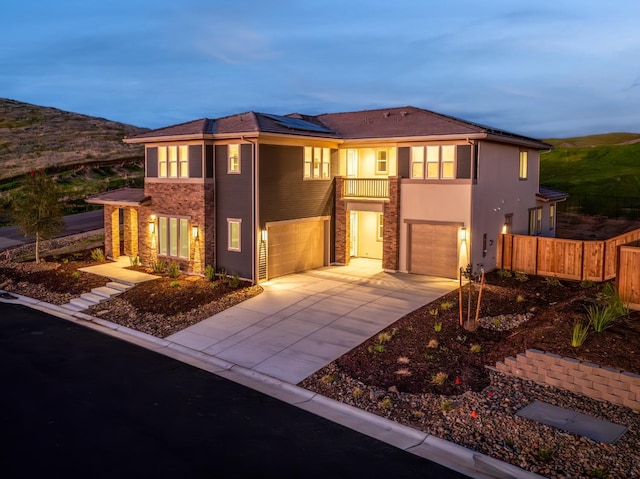view of front of house with solar panels, concrete driveway, an attached garage, fence, and stone siding
