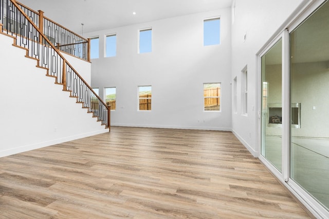 unfurnished living room featuring baseboards, a towering ceiling, light wood finished floors, and stairs