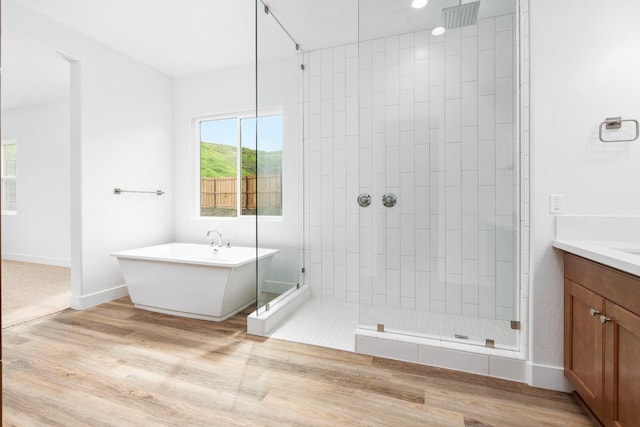 bathroom featuring a shower stall, vanity, wood finished floors, a freestanding tub, and baseboards