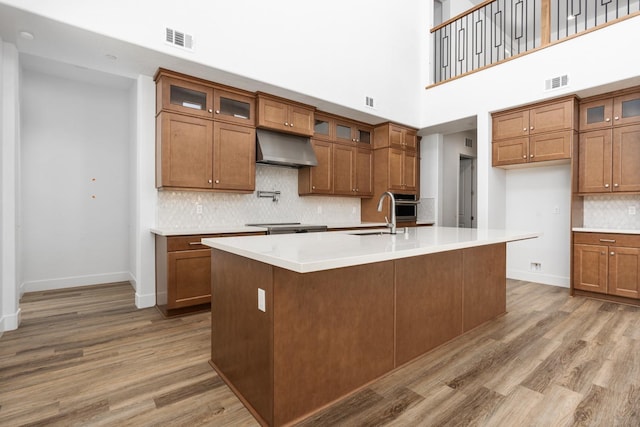 kitchen with visible vents, brown cabinetry, light wood-type flooring, under cabinet range hood, and a sink