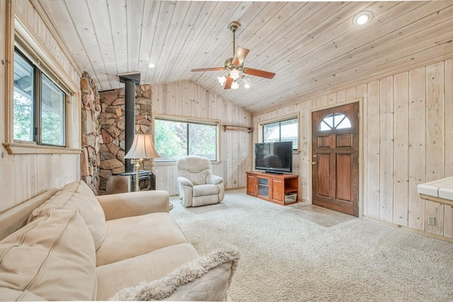 carpeted living area featuring vaulted ceiling, wooden ceiling, a wood stove, and wooden walls