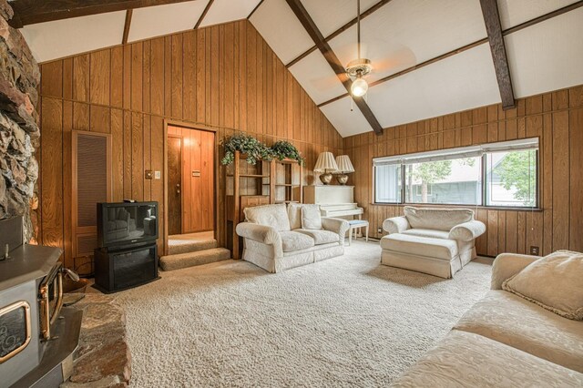 carpeted living area featuring beam ceiling, a wood stove, ceiling fan, wooden walls, and high vaulted ceiling