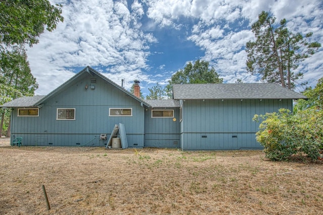 rear view of property with crawl space, a chimney, and roof with shingles