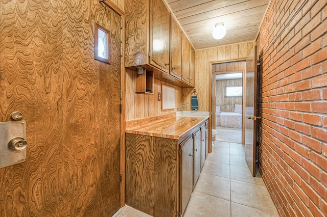 kitchen with light tile patterned flooring, a sink, wood counters, brick wall, and wooden ceiling