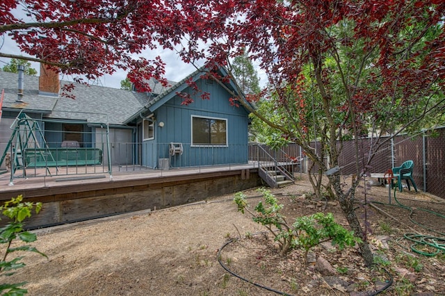 rear view of property with a shingled roof, a chimney, fence, and a deck