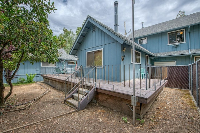 back of house with a shingled roof, a wooden deck, and fence