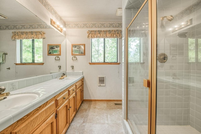 bathroom with heating unit, double vanity, a sink, a shower stall, and baseboards