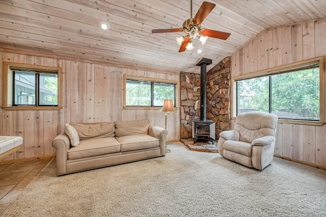 carpeted living room with wood walls, wood ceiling, a ceiling fan, vaulted ceiling, and a wood stove