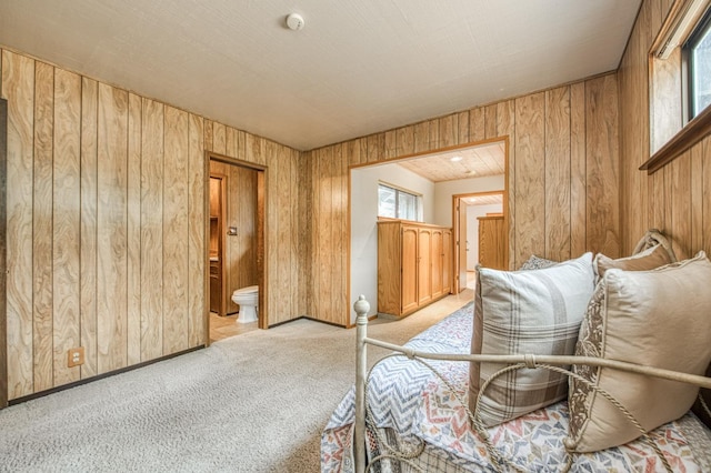 bedroom featuring wooden walls, baseboards, ensuite bathroom, and light colored carpet