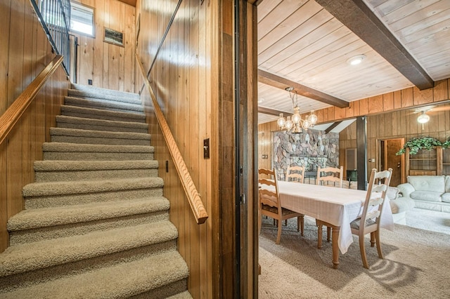 staircase featuring a chandelier, carpet, beam ceiling, and wooden walls