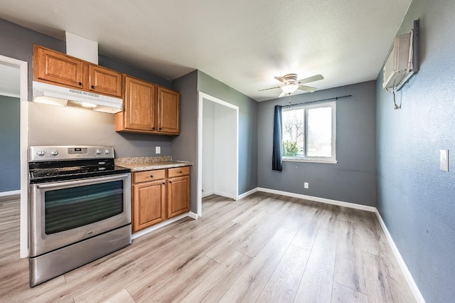 kitchen featuring baseboards, light wood finished floors, stainless steel electric range, an AC wall unit, and under cabinet range hood