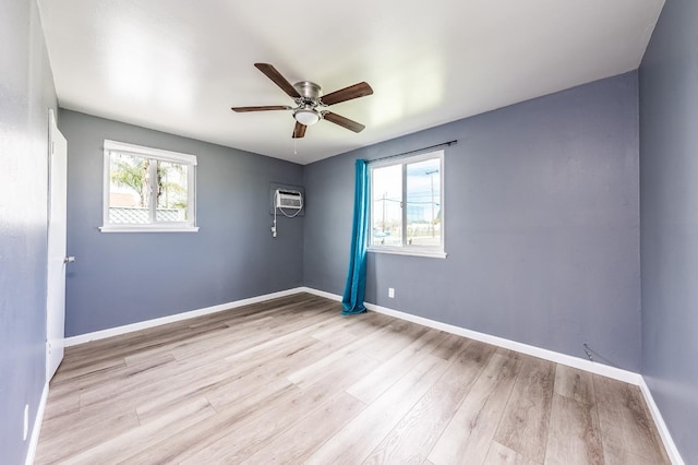 spare room featuring a wall unit AC, wood finished floors, baseboards, and ceiling fan