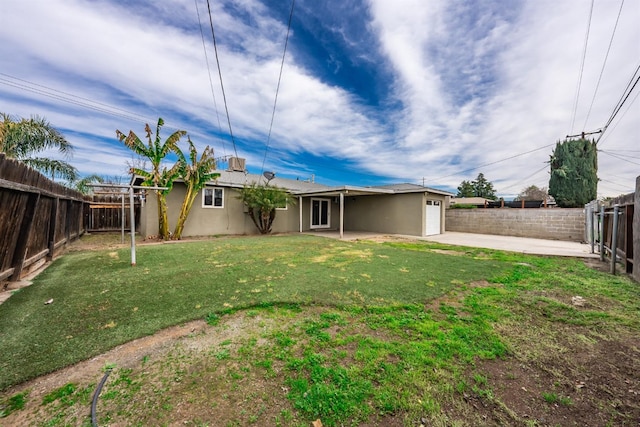 rear view of property with a yard, a fenced backyard, a garage, driveway, and a patio