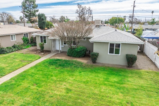 view of front of home with stucco siding, roof with shingles, a front yard, and fence