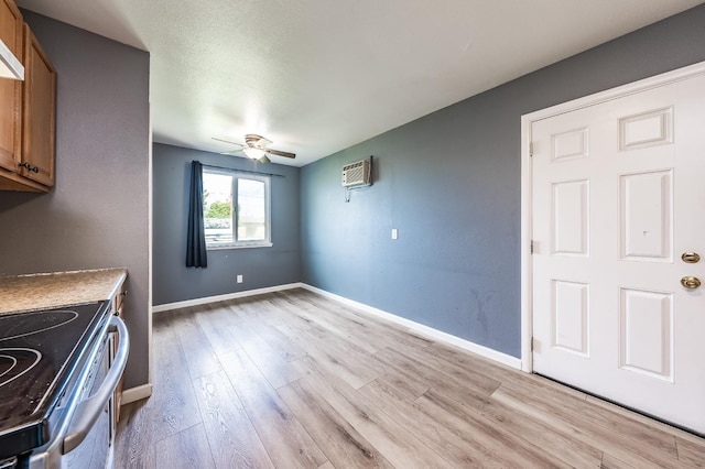 unfurnished dining area with light wood-style flooring, a ceiling fan, baseboards, and a wall mounted air conditioner