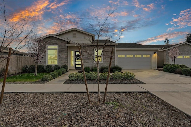 view of front facade with stone siding, driveway, an attached garage, and fence