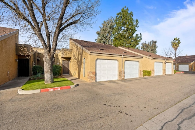 exterior space featuring stone siding, community garages, and stucco siding