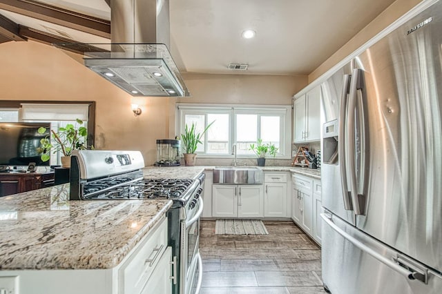 kitchen with visible vents, appliances with stainless steel finishes, white cabinets, a sink, and island range hood