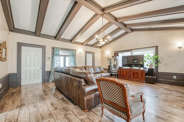 living area with lofted ceiling with beams, wainscoting, light wood-style flooring, and an inviting chandelier