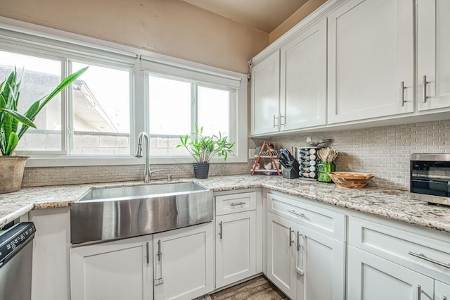 kitchen with decorative backsplash, stainless steel dishwasher, white cabinets, a sink, and light stone countertops