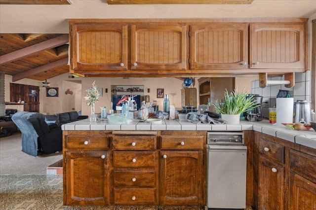 kitchen with tile counters, brown cabinets, open floor plan, vaulted ceiling with beams, and a peninsula