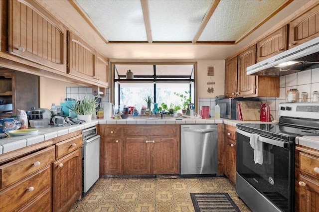 kitchen featuring stainless steel appliances, tasteful backsplash, brown cabinets, and under cabinet range hood