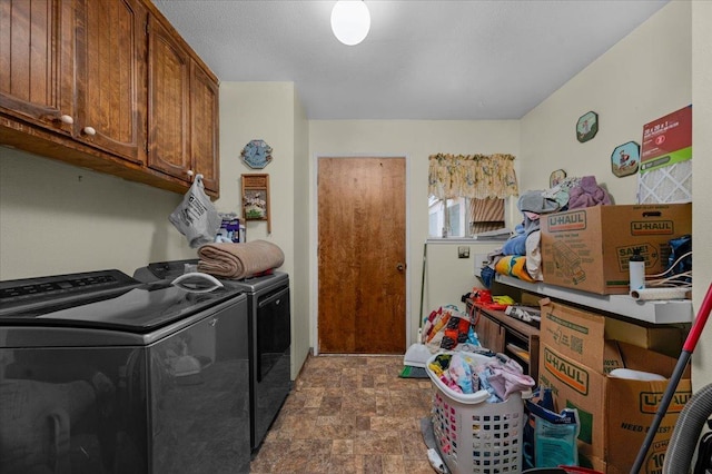 clothes washing area featuring cabinet space, stone finish floor, and washing machine and clothes dryer