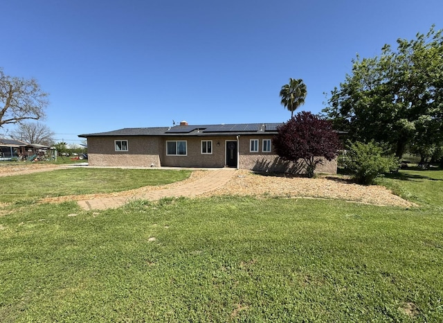 back of property featuring stucco siding, a lawn, and roof mounted solar panels