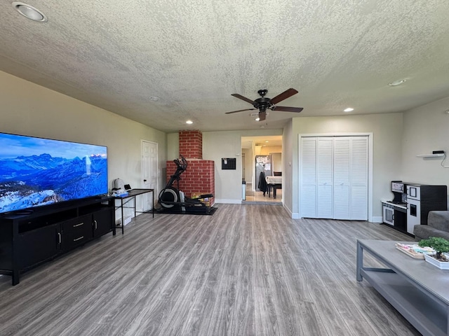 living room featuring a textured ceiling, wood finished floors, ceiling fan, and baseboards