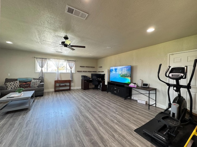 living room featuring baseboards, a textured ceiling, visible vents, ceiling fan, and wood finished floors