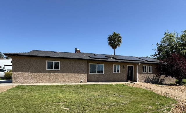 single story home with stucco siding, solar panels, and a front yard