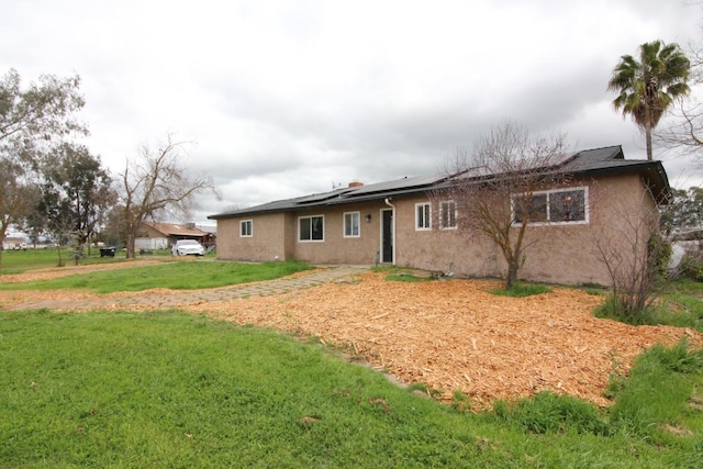 rear view of house featuring a lawn, stucco siding, and roof mounted solar panels