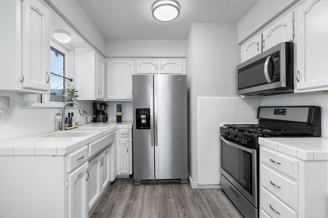 kitchen with tile countertops, appliances with stainless steel finishes, light wood-style floors, white cabinetry, and a sink