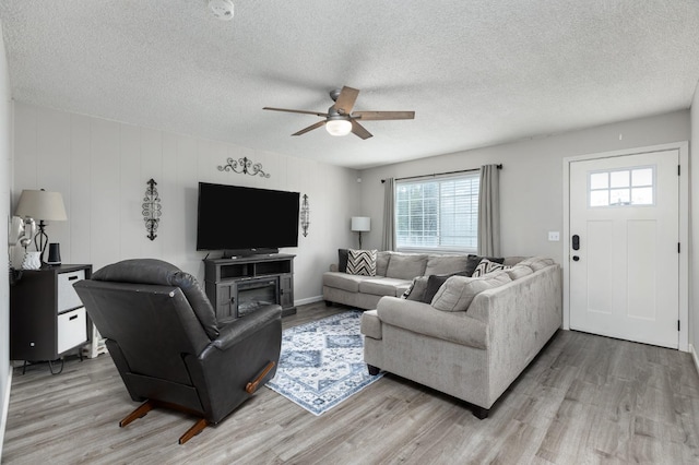 living area featuring light wood finished floors, ceiling fan, and a textured ceiling